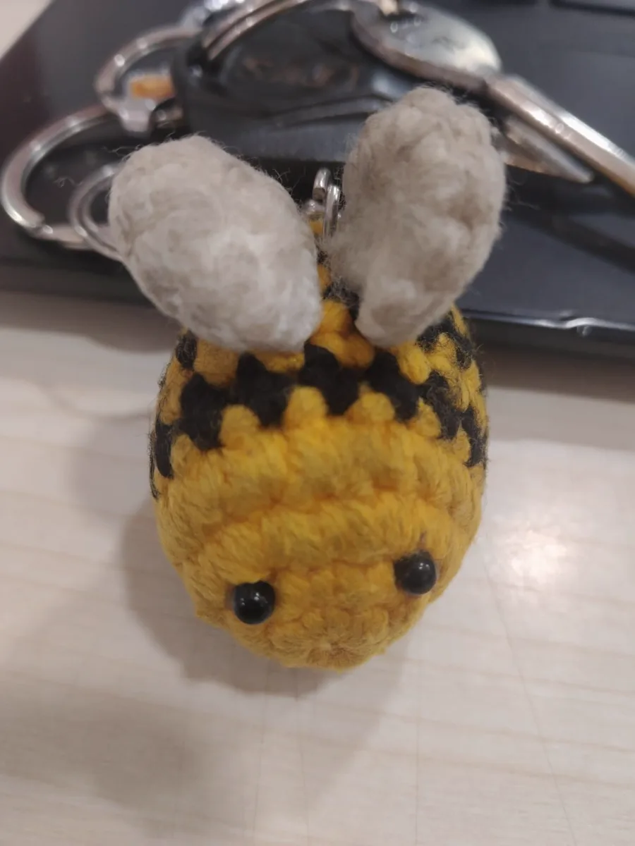 Original phone photo of a crochet bee keychain on a cluttered desk